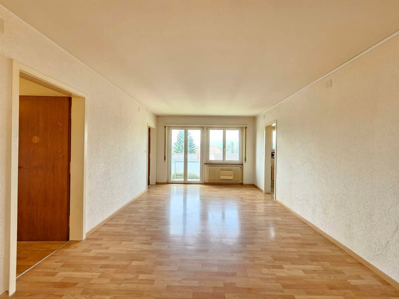 Empty room, wooden floor, white walls, glass doors leading to balcony, radiators, sliding windows, door