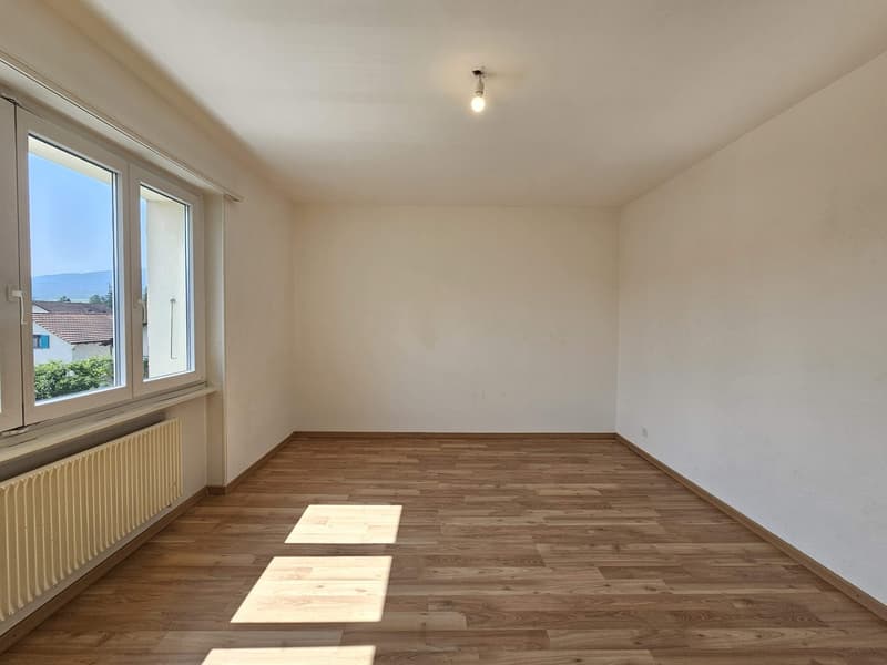 Spacious bedroom with hardwood flooring, white walls, and a single window providing natural light. The room appears to be empty, ready for furnishing and personalization.