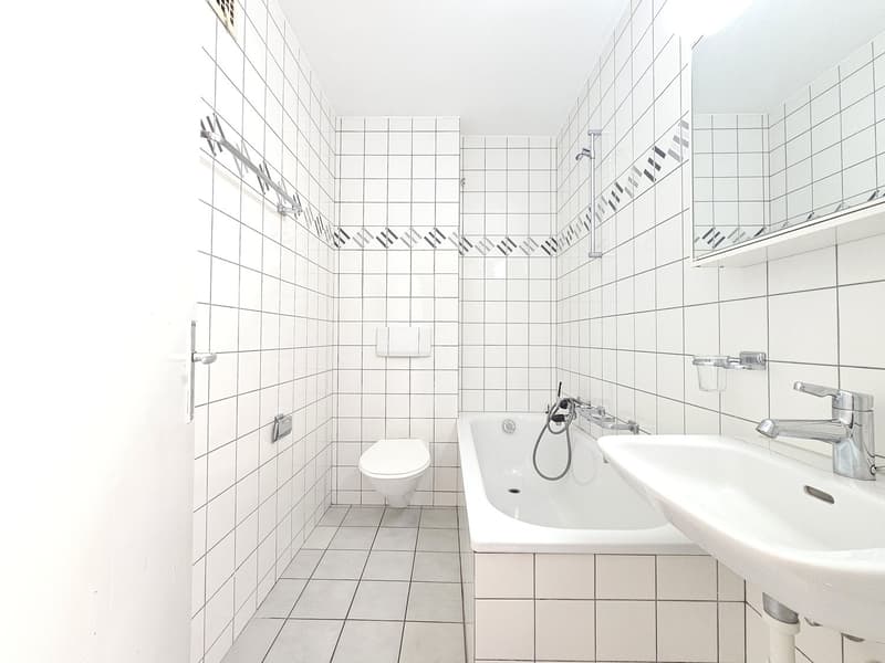 Tiled bathroom with white walls and floors, a toilet, a sink, and a shower area.
