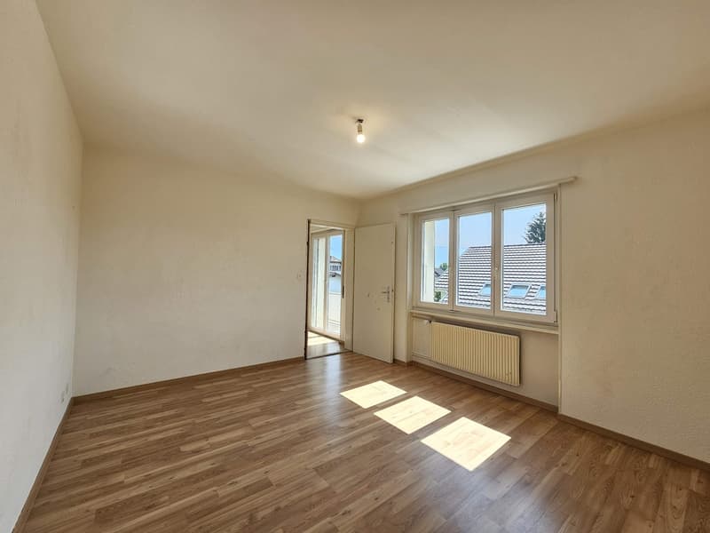 Spacious room with hardwood flooring, white walls, and large windows providing natural light. The room appears to be empty, ready for furnishing and decorating.