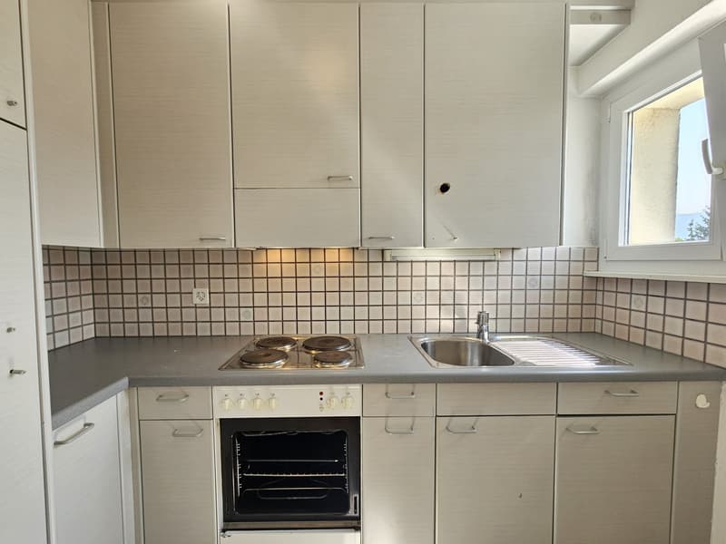 The image shows a kitchen with white cabinets, a tiled backsplash, a stove with four burners, and a sink. There appears to be a dishwasher visible in the kitchen as well.