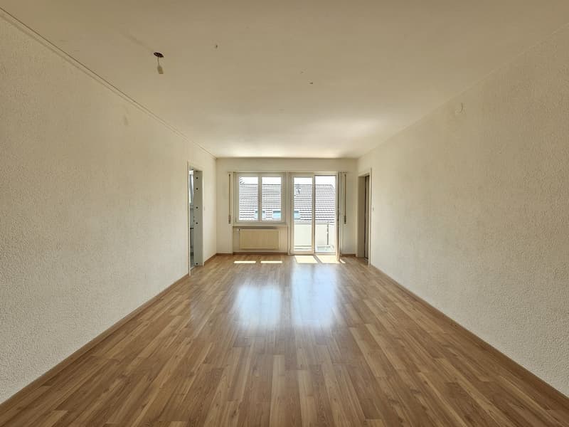 Spacious living room with hardwood flooring, large windows, and a radiator. The room appears to be empty, providing a blank canvas for furnishing and decorating.
