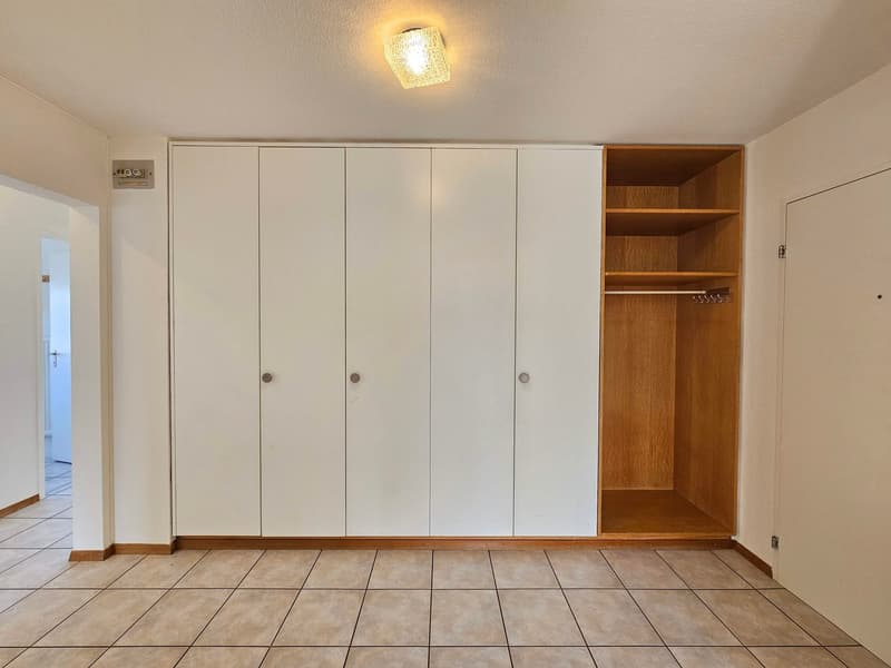 Empty room with white cabinets and wooden shelf, square tile flooring, white walls, light on the ceiling