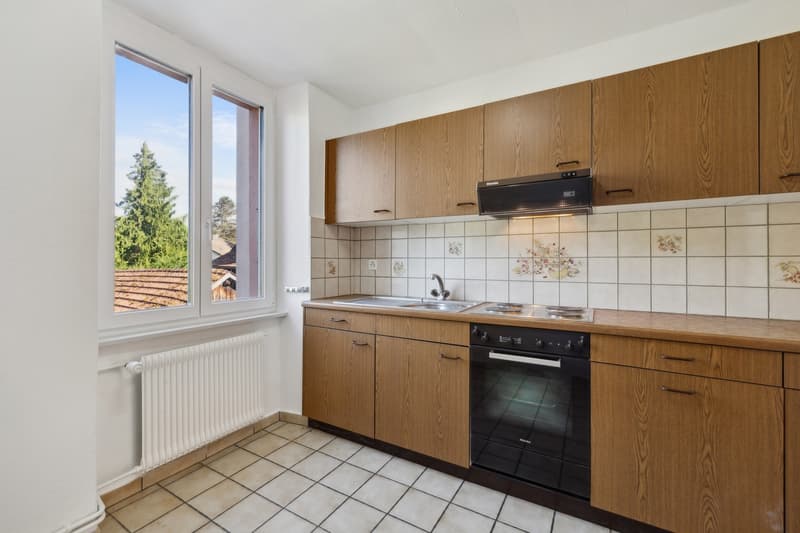 Spacious kitchen with wooden cabinets, tiled backsplash, electric stove, and dishwasher. Large windows provide natural light and a view of the outdoors.