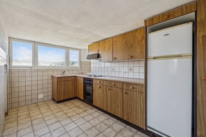Spacious kitchen with wooden cabinets, tiled floor, oven, refrigerator, and large windows providing natural light
