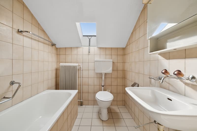 Tiled bathroom with a bathtub, toilet, sink, and radiator. The room has a skylight providing natural light.
