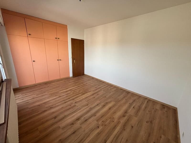 The image shows a bedroom with a wooden floor, white walls, and a built-in wardrobe with orange doors. The room appears to be empty and ready for furnishing.