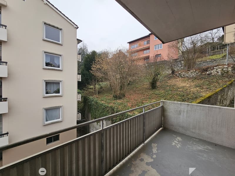 Apartment building with balconies, surrounded by trees and vegetation on a hillside