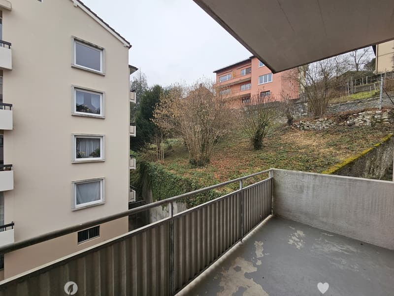 Apartment building with balconies, surrounded by trees and vegetation on a hillside