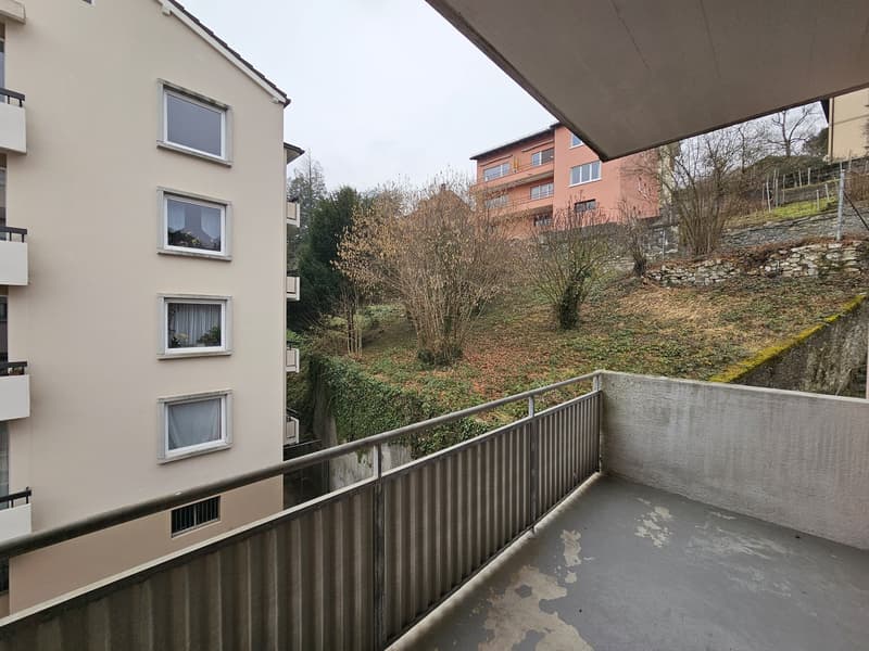 Apartment building with balconies, surrounded by trees and vegetation on a hillside