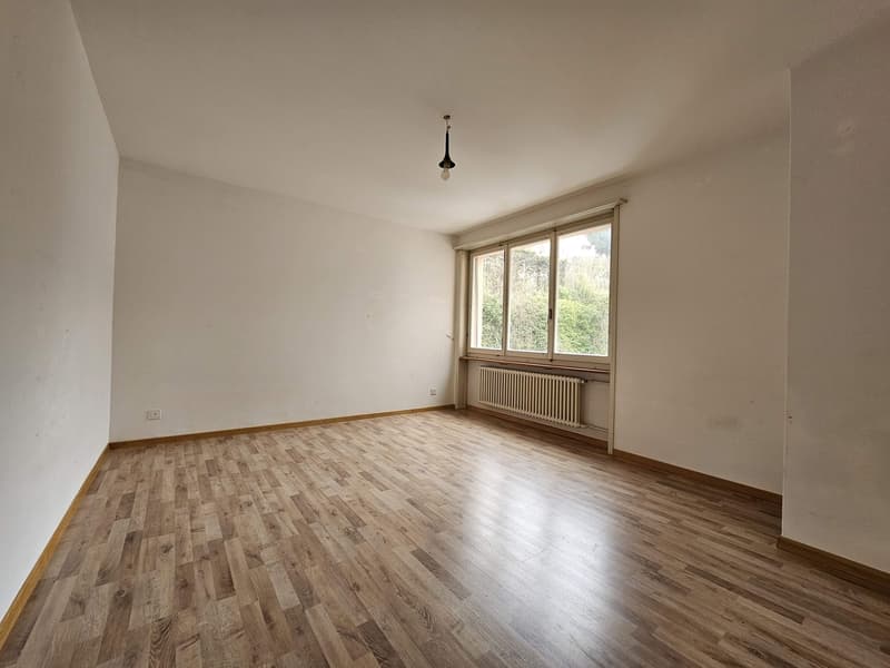 Spacious room with hardwood flooring, white walls, and a large window overlooking the outdoors. The room appears to be empty, ready for furnishing and decorating.