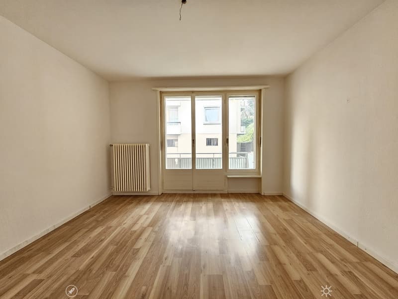 Spacious living room with hardwood floors, large windows, and a radiator. The room appears to be empty, ready for furnishing and decorating.