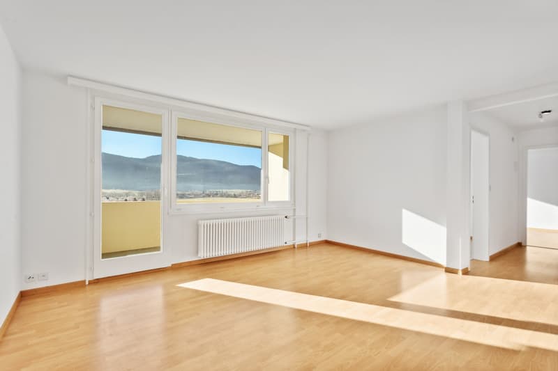 Spacious living room with large windows offering a scenic view of the mountains, hardwood flooring, and a bright, airy atmosphere.