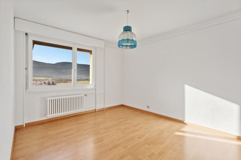 Spacious bedroom with large windows offering a scenic view of the mountains, hardwood flooring, and a decorative blue and white pendant light fixture.
