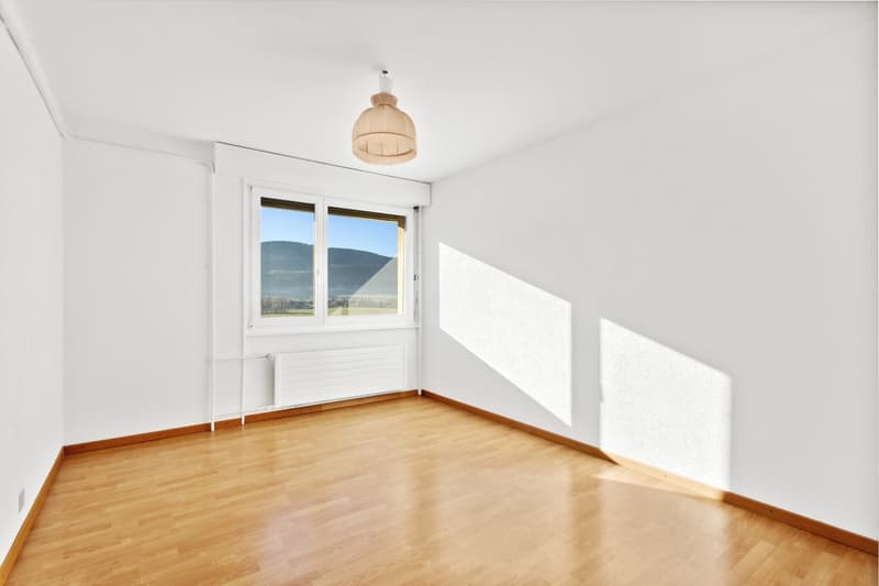 Spacious bedroom with large windows offering a scenic view, hardwood flooring, and a wooden pendant light fixture.