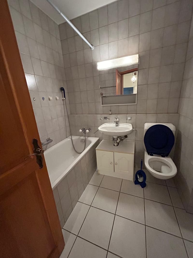 Tiled bathroom with a bathtub, sink, and toilet. There is a cabinet under the sink and a mirror on the wall.