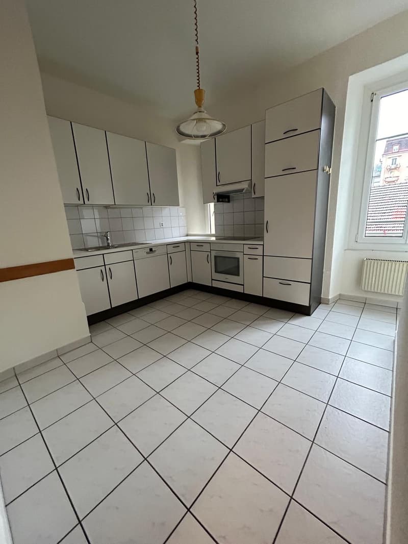 Spacious L-shaped kitchen with white cabinets, tiled floor, and a dishwasher