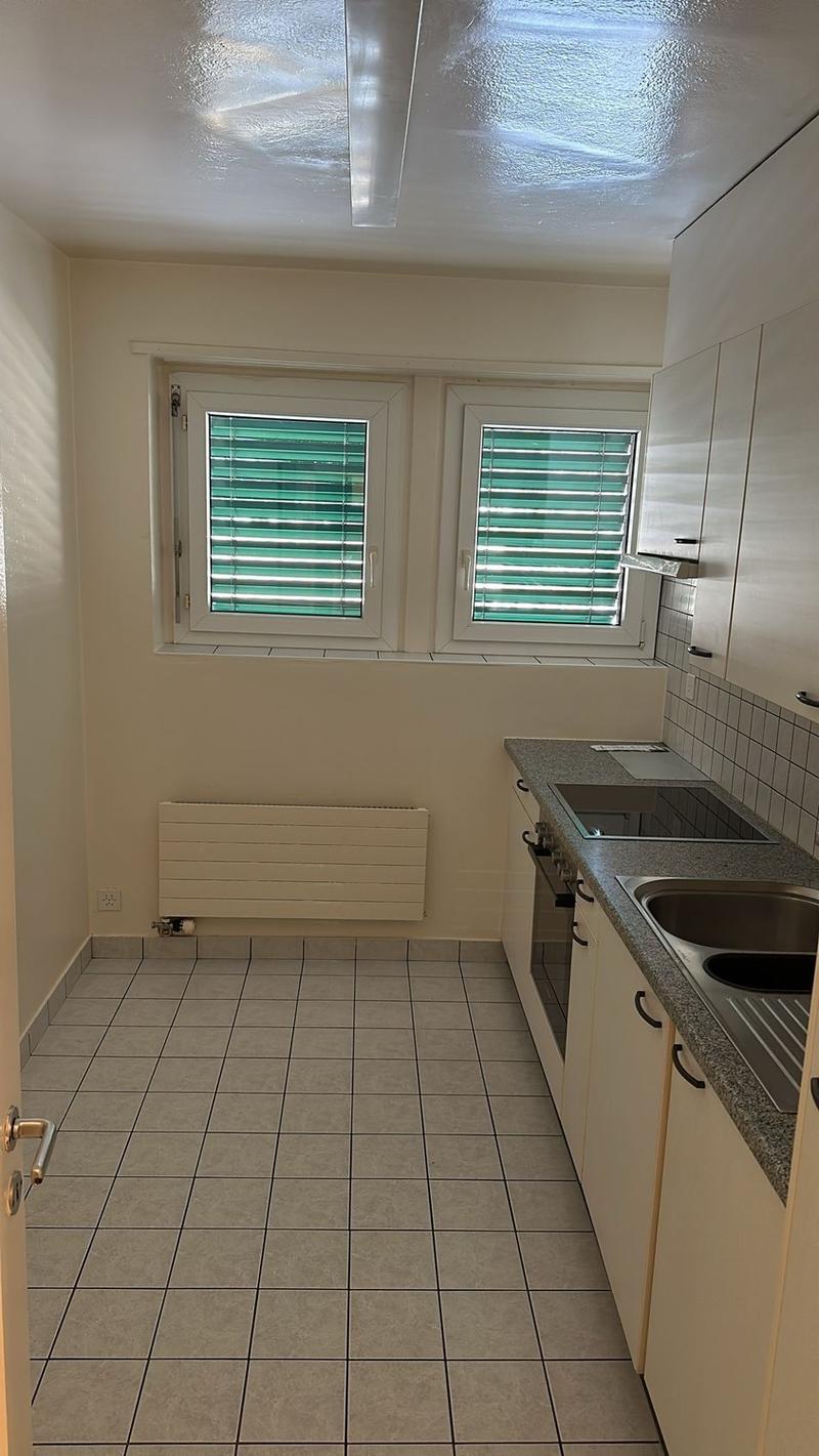 Tiled floor, white walls, windows with green blinds, kitchen counter with sink and dishwasher