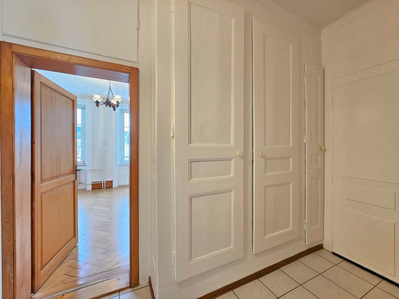 Empty room, white walls, wooden door, parquet floor, and closed doors.