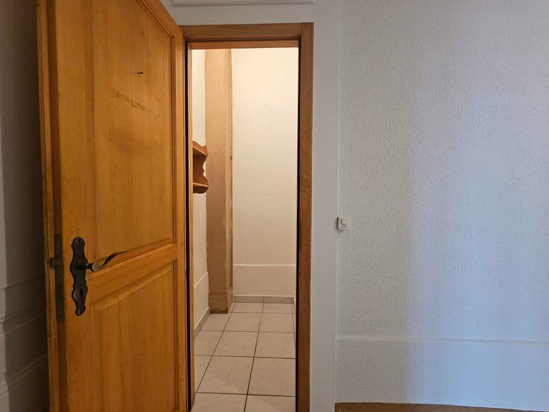 Open door leading to hallway with tiled floor, small window, white walls