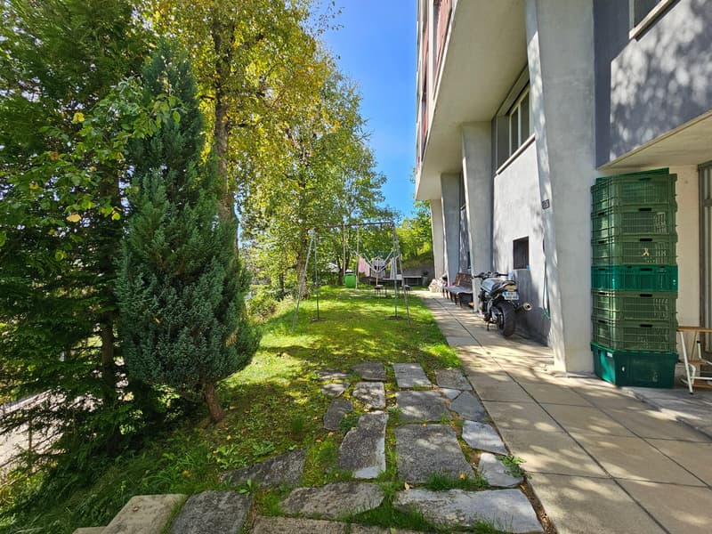 a courtyard of a building with a lawn and trees, a stack of green crates, a swing and some benches