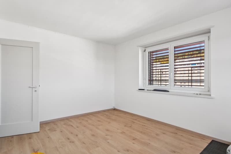 an empty room with wooden floor, white walls, white door, and a window with blinds