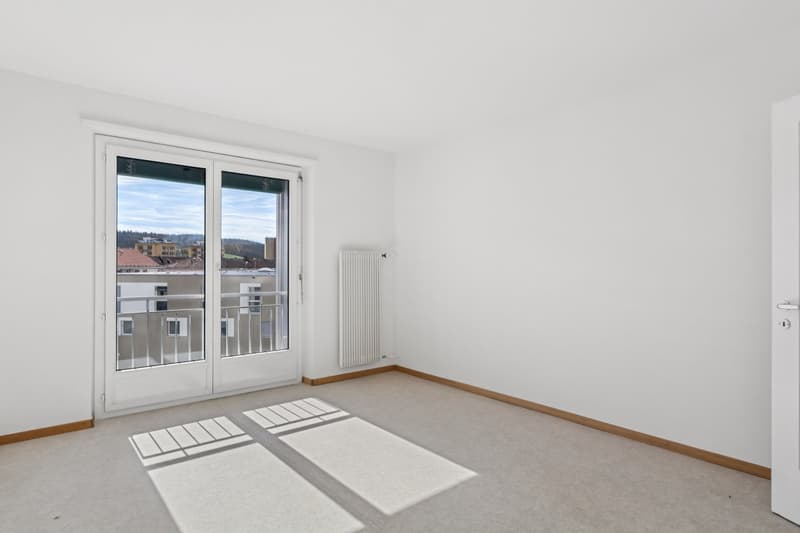 Empty room with sliding glass doors, balcony with railings, white walls, white ceiling, and radiator.