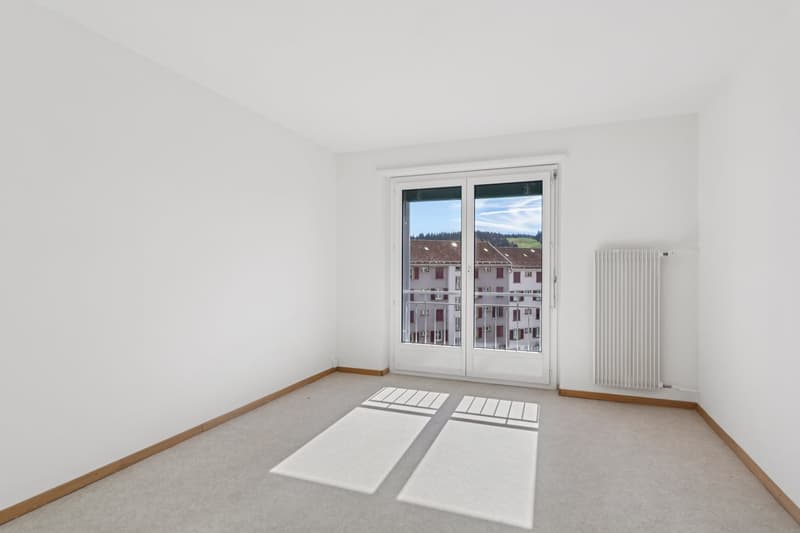 White walls, sliding glass doors leading to balcony, carpet floor, white radiator