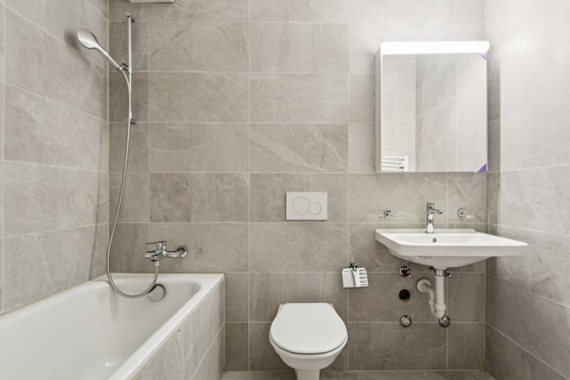 White bathtub, white toilet, white sink, wall mounted mirror, wall tiles, faucet