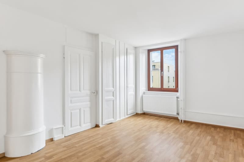 Empty room with white walls, wooden floor, white radiator, and window
