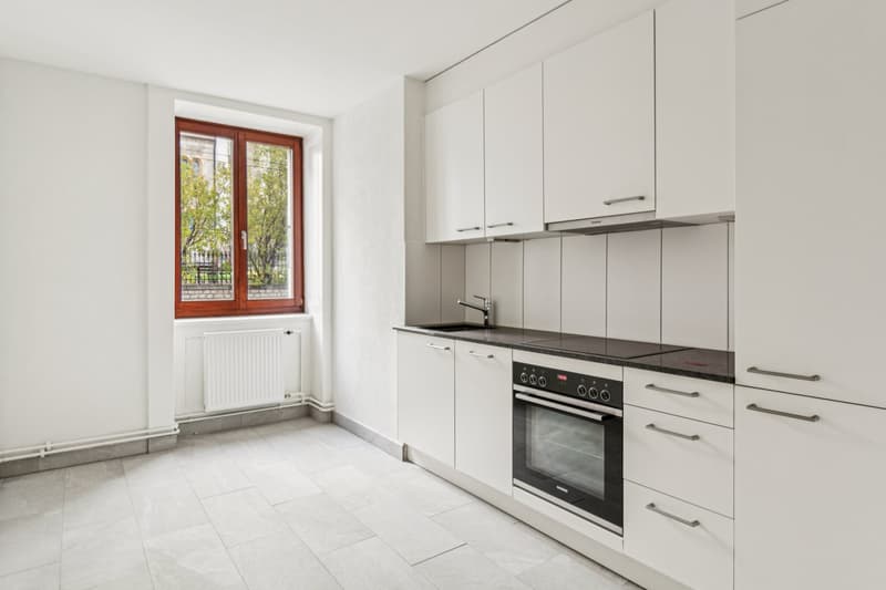 Kitchen with white cabinets, black countertops, white tile flooring, modern white oven and sink with a faucet, and a window with view outside.