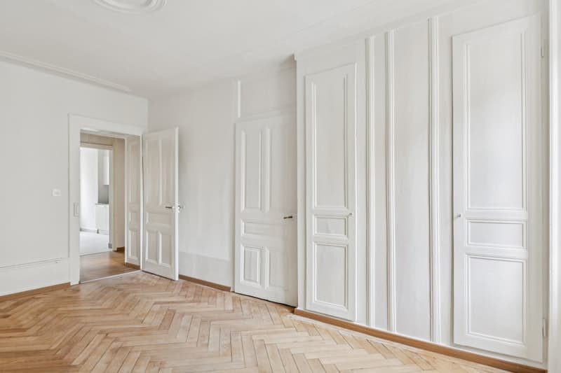 empty room, white walls, wooden herringbone floor, three doors, no furniture