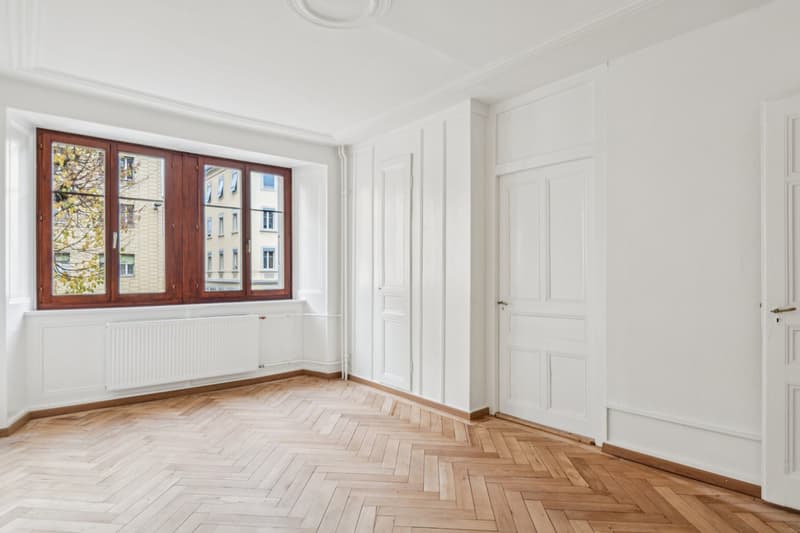 Empty room with white walls, wooden floor, windows with radiator, doors