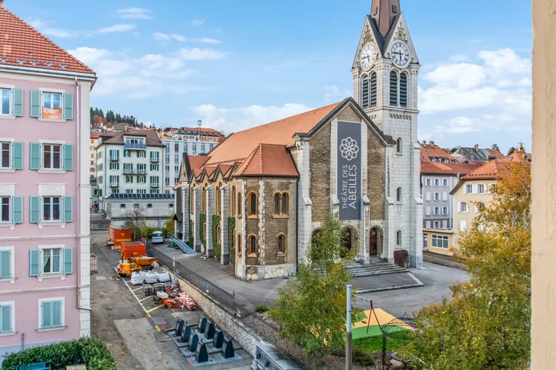 exterior view of a church building with a tall clock tower and red rooftop, with nearby construction materials and vehicles