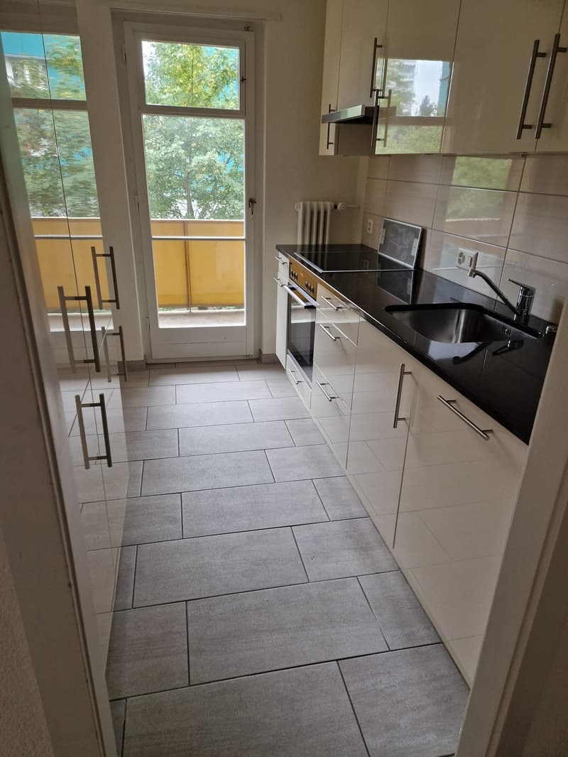 modern kitchen, white cabinets, black countertops, stainless steel sink, gas stove, integrated oven, white tiled flooring