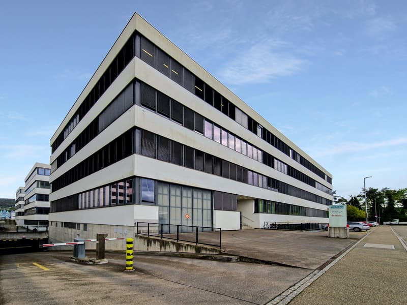 modern office building, concrete exterior, glass windows, multiple floors, parking area, entrance ramp