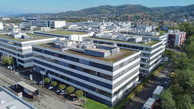 Multi-story office building with large windows, parking spaces, green roofs, green spaces