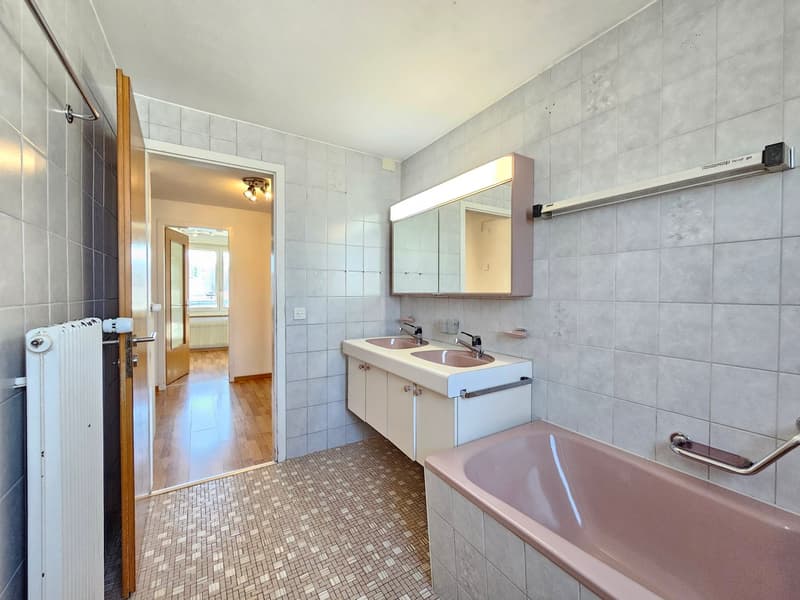 Bathroom with double sink, mirror, bathtub, and radiator