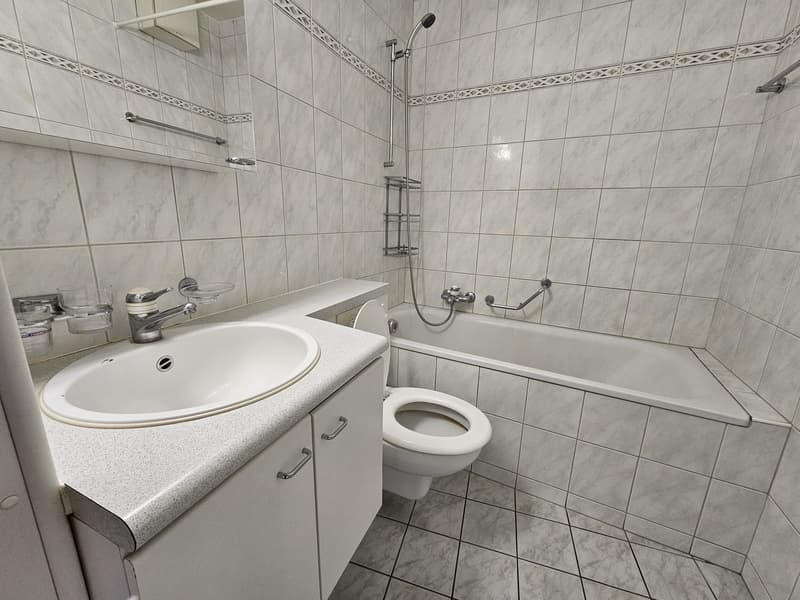 white tiled bathroom with sink, toilet, bathtub, and shower