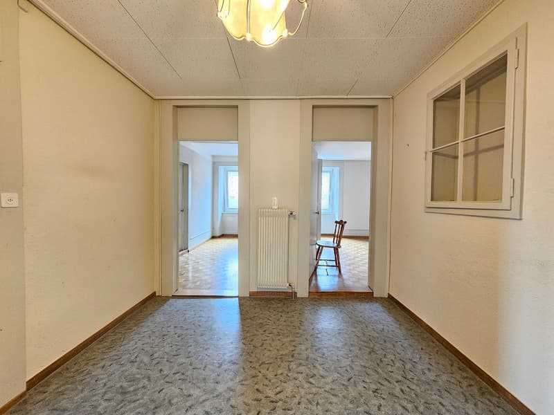 Hallway with 3 doors, radiator, gray floor, light ceiling, white walls