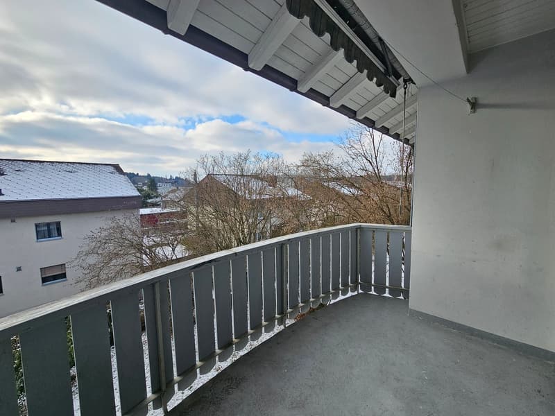 A balcony with gray railings and flooring under a tiled roof