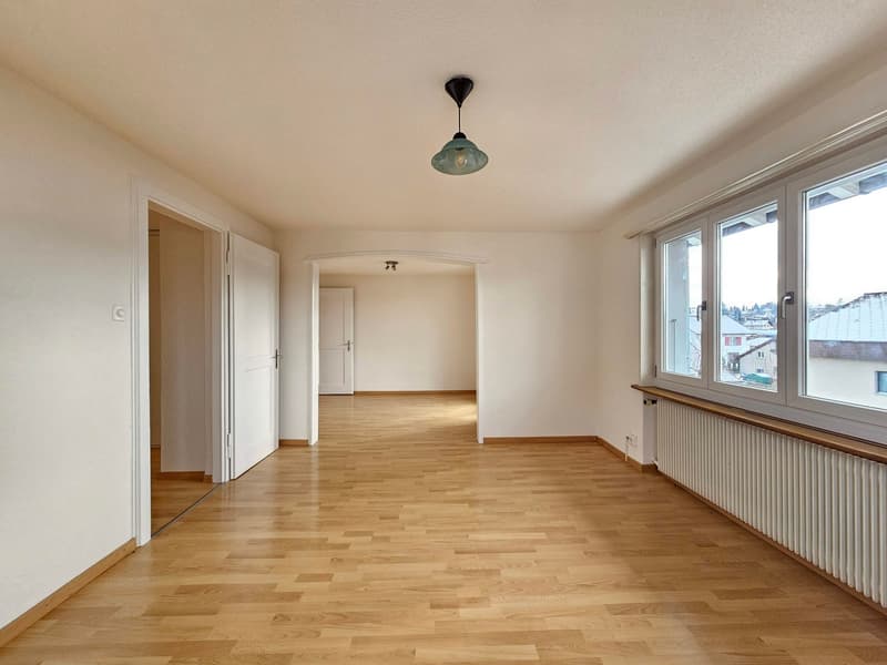 empty room, wooden floor, white walls, two white doors, large windows, hanging lamp, heater