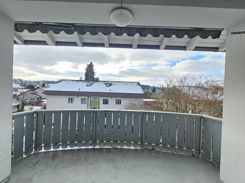 View from a balcony with railings, snow-covered rooftops, trees, and buildings in the distance