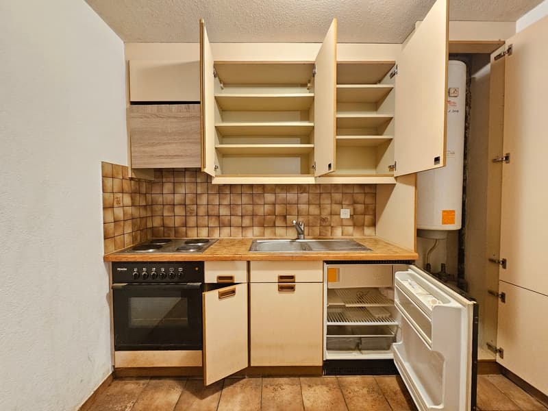 Open cupboards, sink, stove, fridge, cabinets, tile backsplash, wooden floors