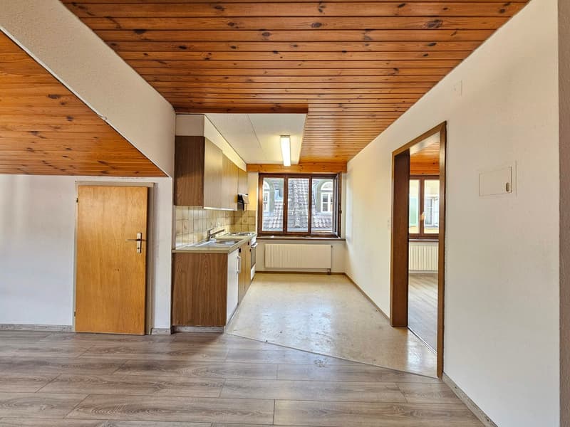 An empty kitchen with wooden cabinets, tiled floor, wooden ceiling, and a sink with faucet.