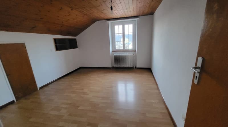 empty room with wooden floors, white walls, wooden door, wooden beam ceiling, window with radiator, small window in wall