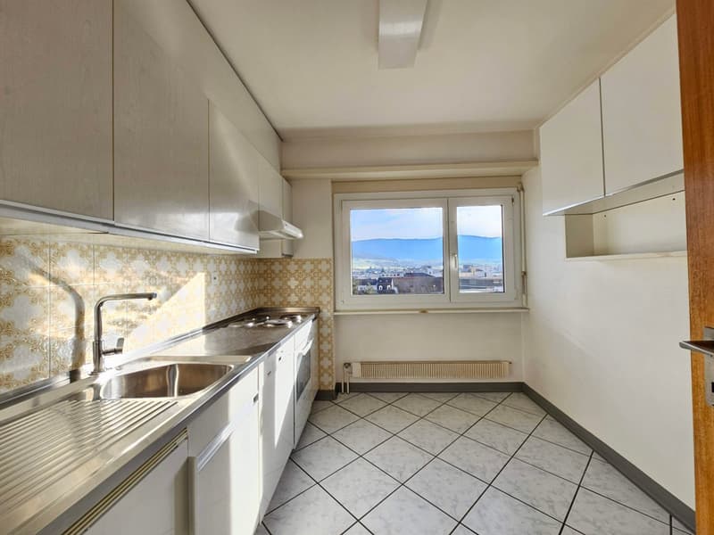 Modern white kitchen with sink, oven, tiled floor, and window with a city view