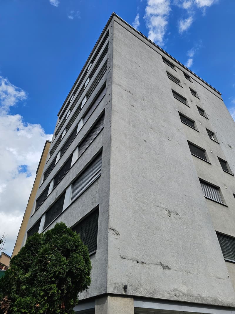 Multi-story building, many windows, grey exterior, small tree