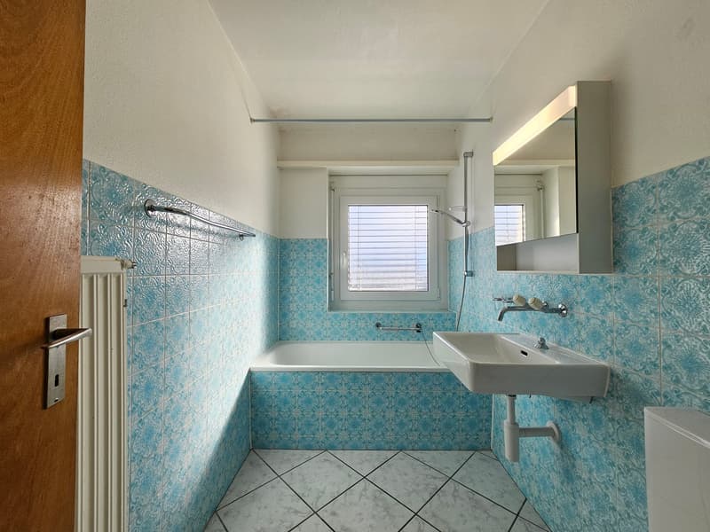 White bathtub, white sink, blue tiles, mirror, white door, toilet