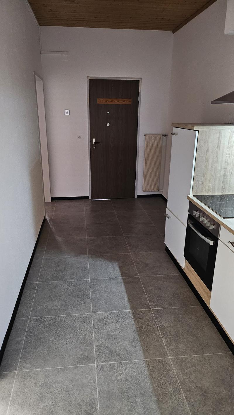 Modern kitchen with white cabinets, tiled floor, wooden ceiling, white walls, built-in oven, and a radiator